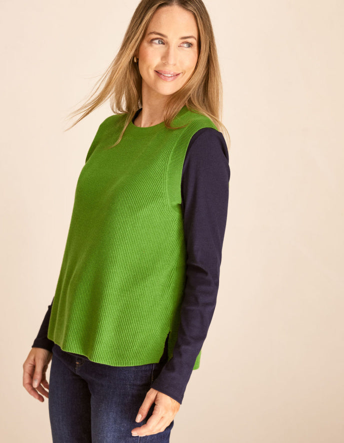 Woman wearing a green cotton tank top over a dark long-sleeve shirt on a beige background