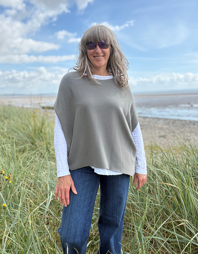 Woman wearing green slate grey tank top with relaxed fit over a white t shirt on a beach and blue sky in the background