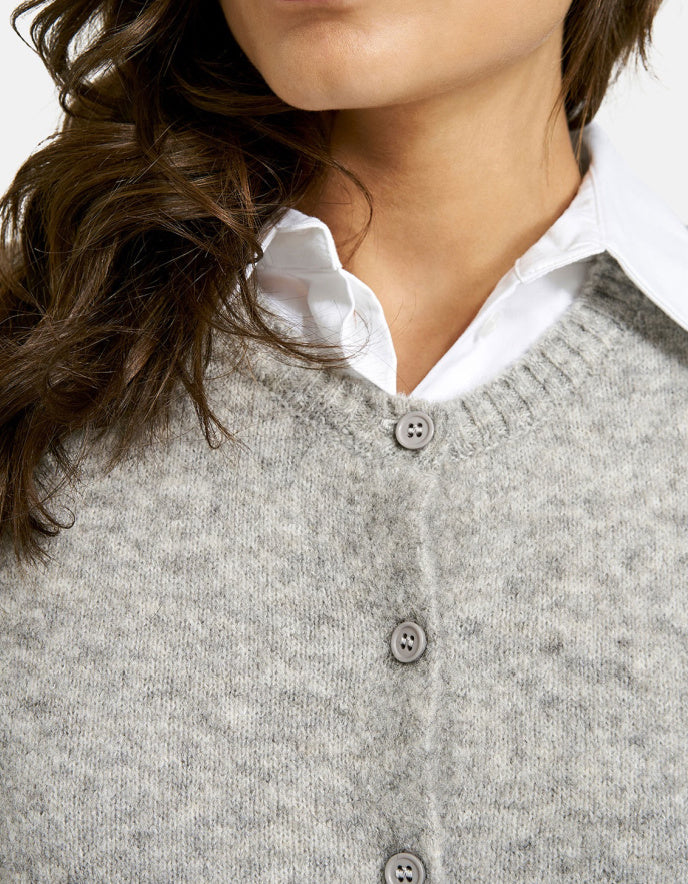 Close-up of a person wearing a gray button-up cardigan over a white shirt.