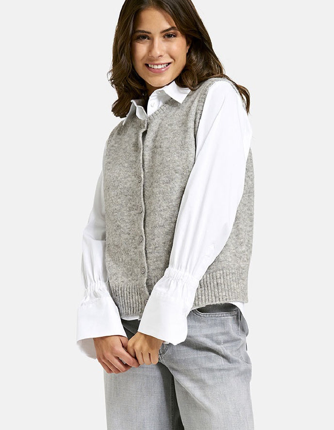 Woman wearing a gray sweater vest over a white shirt on a white background