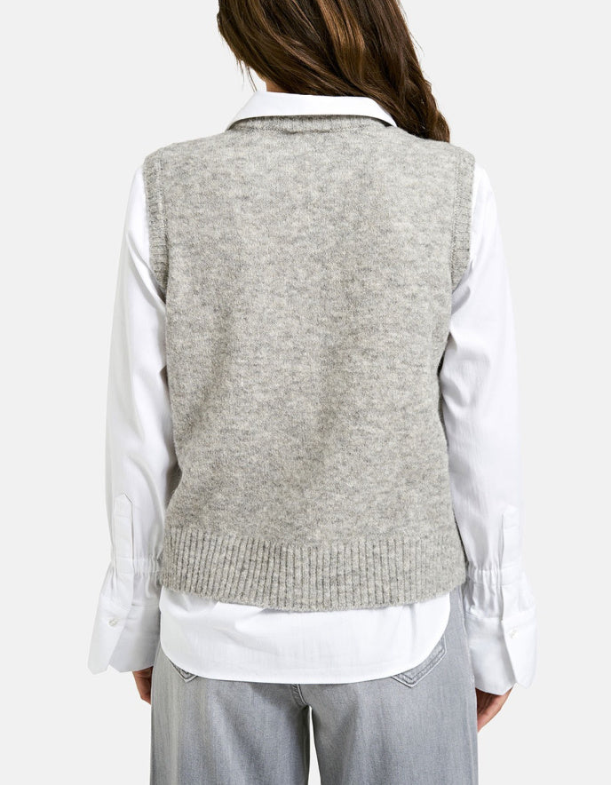 Person wearing a light gray sweater vest over a white shirt on a plain background
