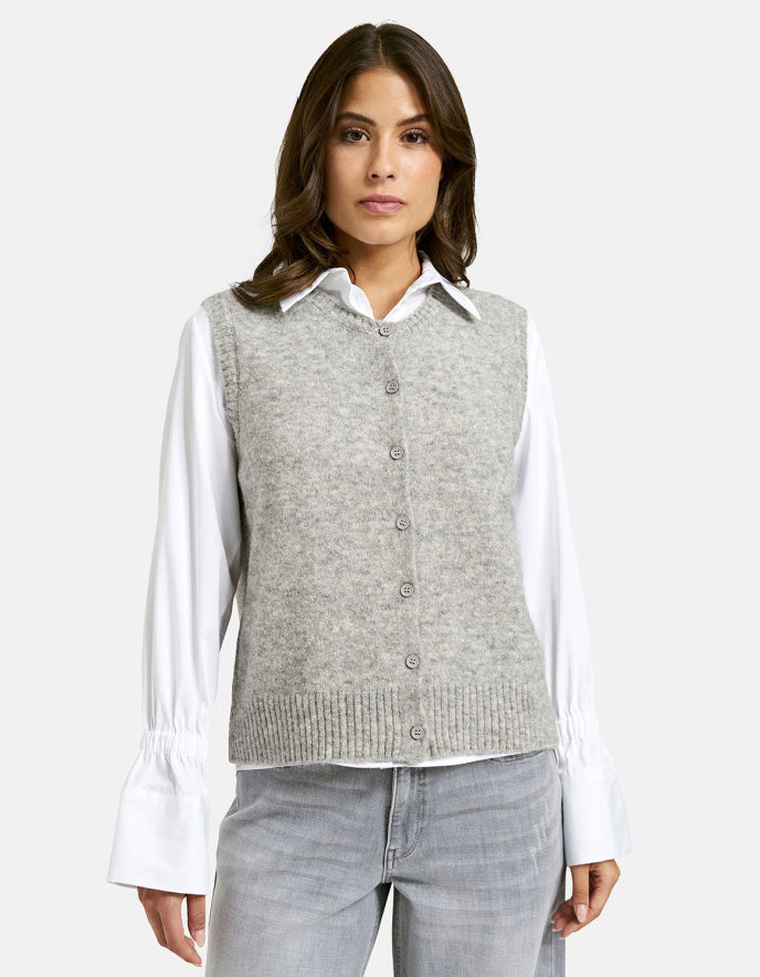 Woman wearing a gray sweater vest over a white shirt on a light gray background