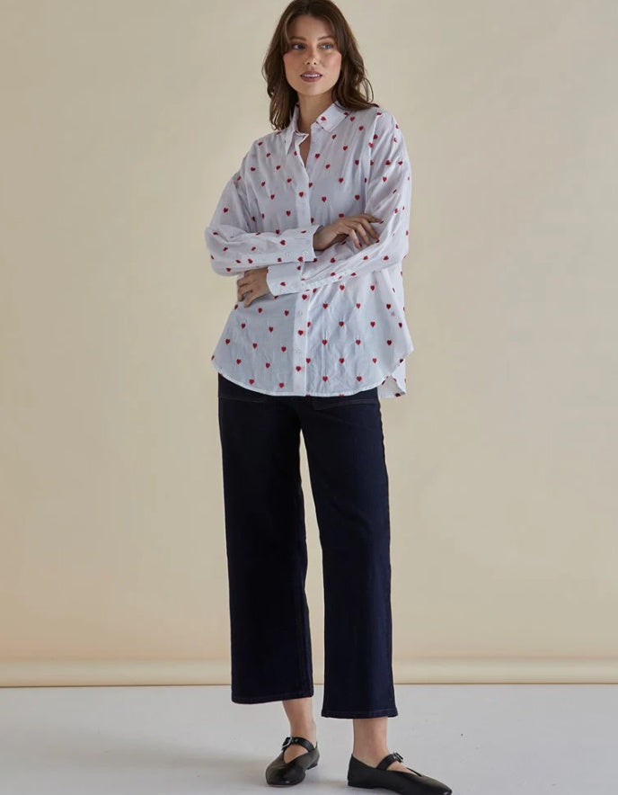 Woman wearing a white blouse with red patterns and black pants against a beige background