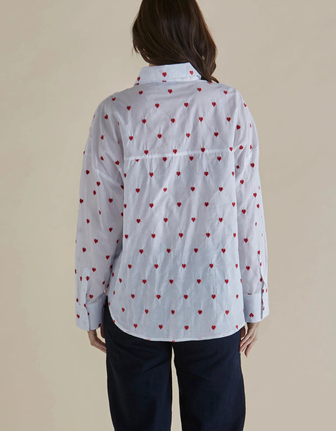 Person wearing a light blue shirt with red heart patterns on a beige background