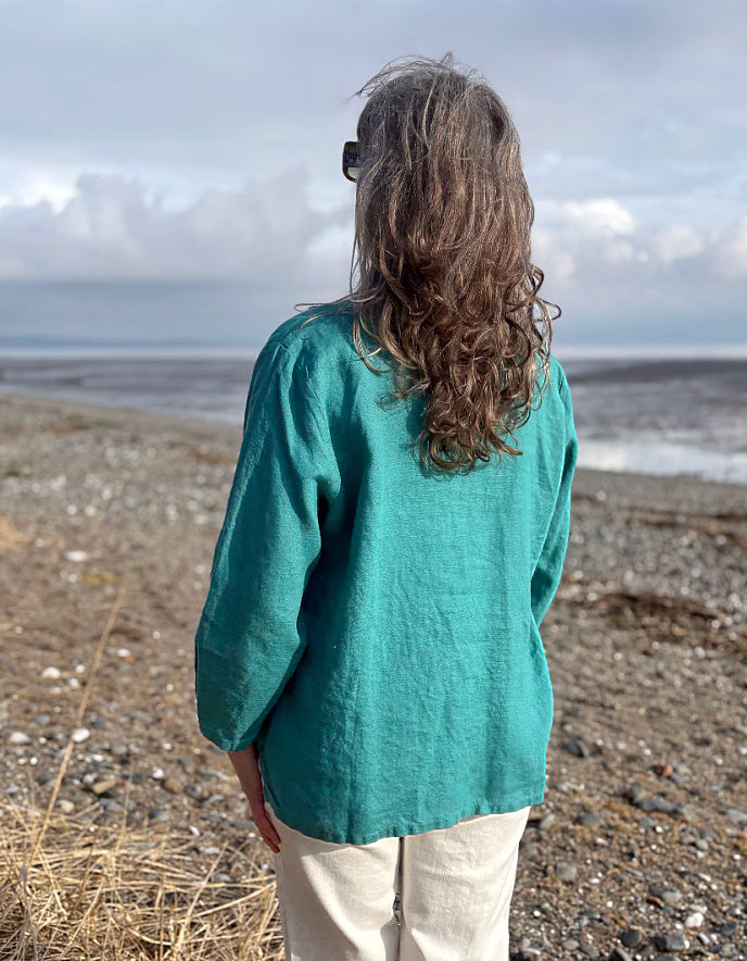 Person wearing a teal shirt standing on a beach with a cloudy sky.