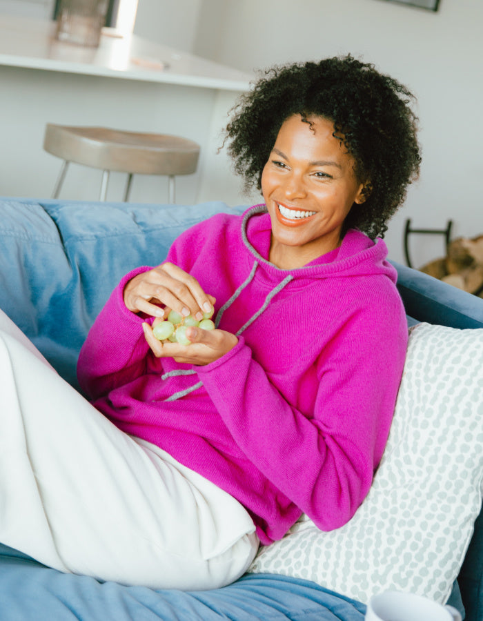 Woman in pink hoodie holding grapes on a blue couch