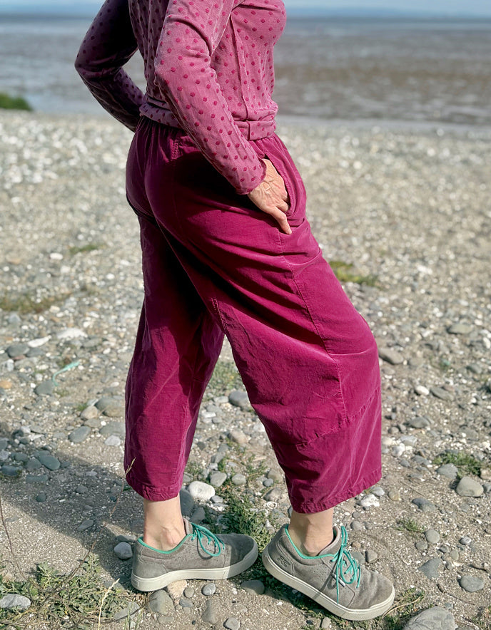 Woman in pink needlecord lantern trousers and a pink pink spotty top standing on a pebbly beach with ocean and sky in the background