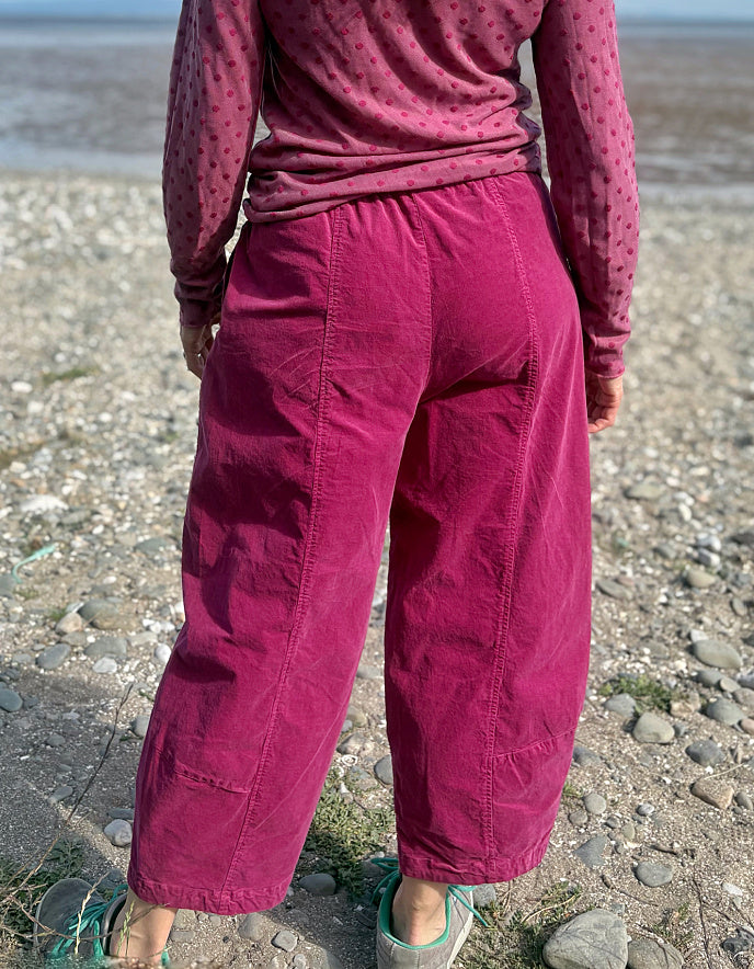 Woman in pink needlecord lantern trousers and a pink pink spotty top standing on a pebbly beach with ocean and sky in the background
