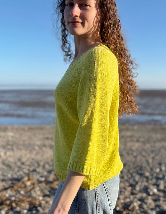 Woman wearing a yellow sweater standing on a beach with ocean in the background