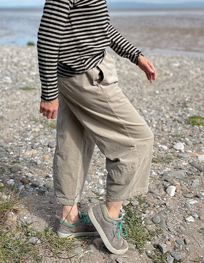 Person wearing a striped shirt and beige pants on a pebbly beach.