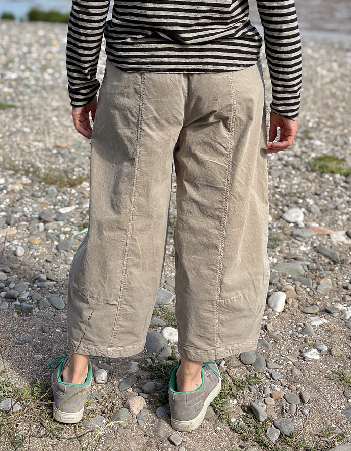 Person wearing beige pants and a striped shirt standing on a rocky ground.