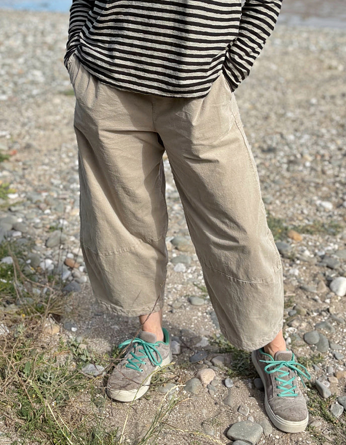 Person wearing a striped shirt, beige lantern cord pants, and sneakers on a rocky ground.