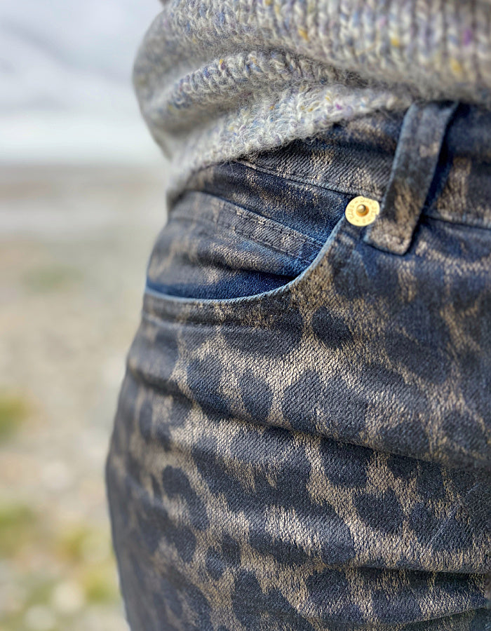Close-up of a person wearing leopard print jeans with a blurred natural background
