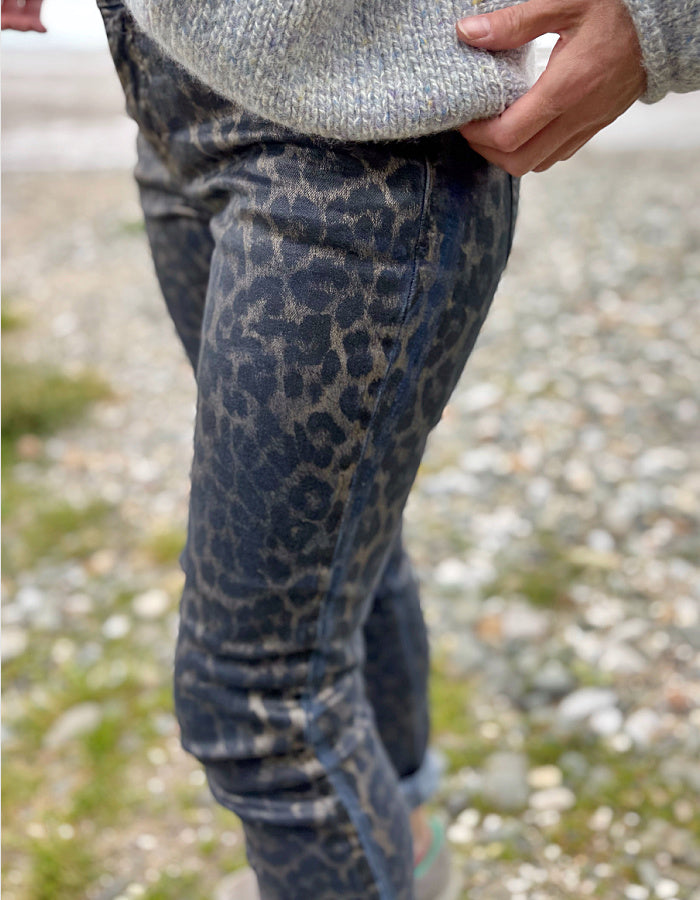 Person wearing leopard print pants and a gray sweater on a blurred natural background