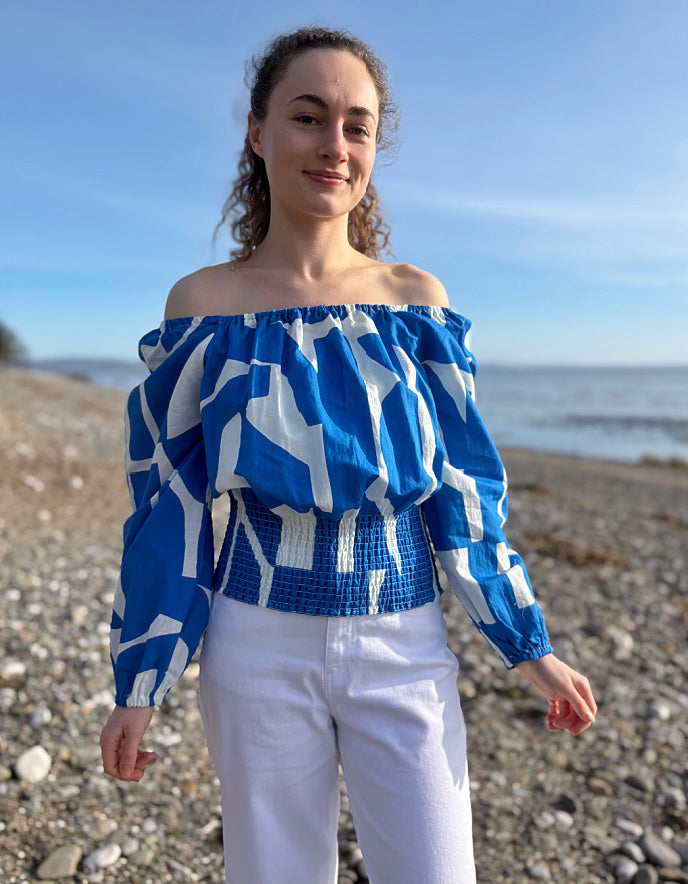 Woman wearing a blue and white patterned top on a pebbly beach.