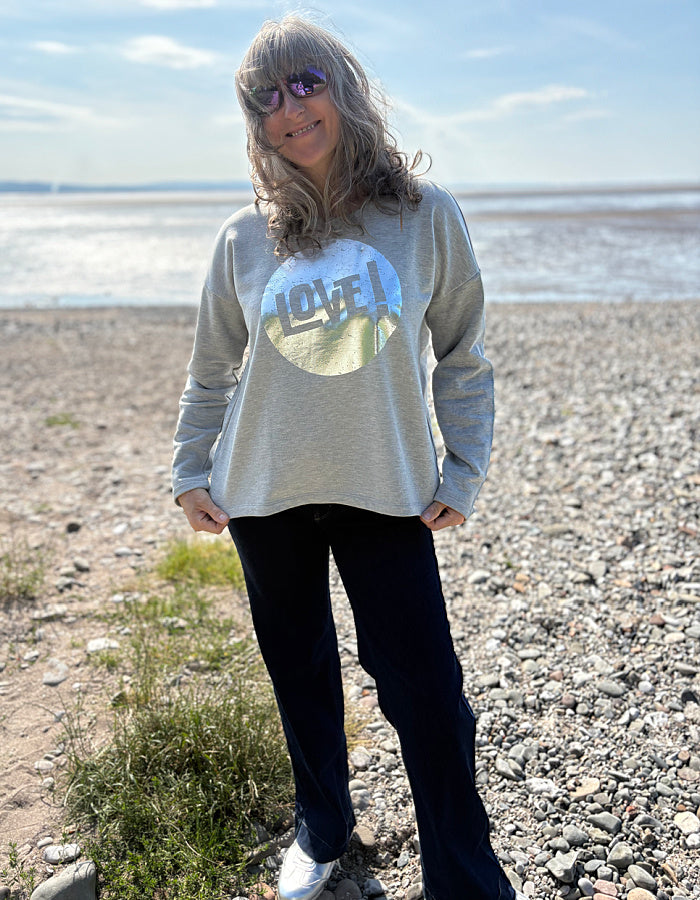 Person wearing a sweatshirt with a 'lovel' graphic design on a beach.