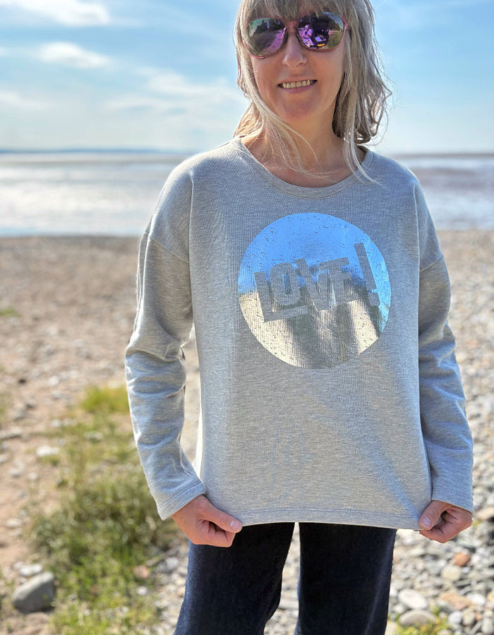 Person wearing a grey cotton sweatshirt with a silver graphic design that says LOVE