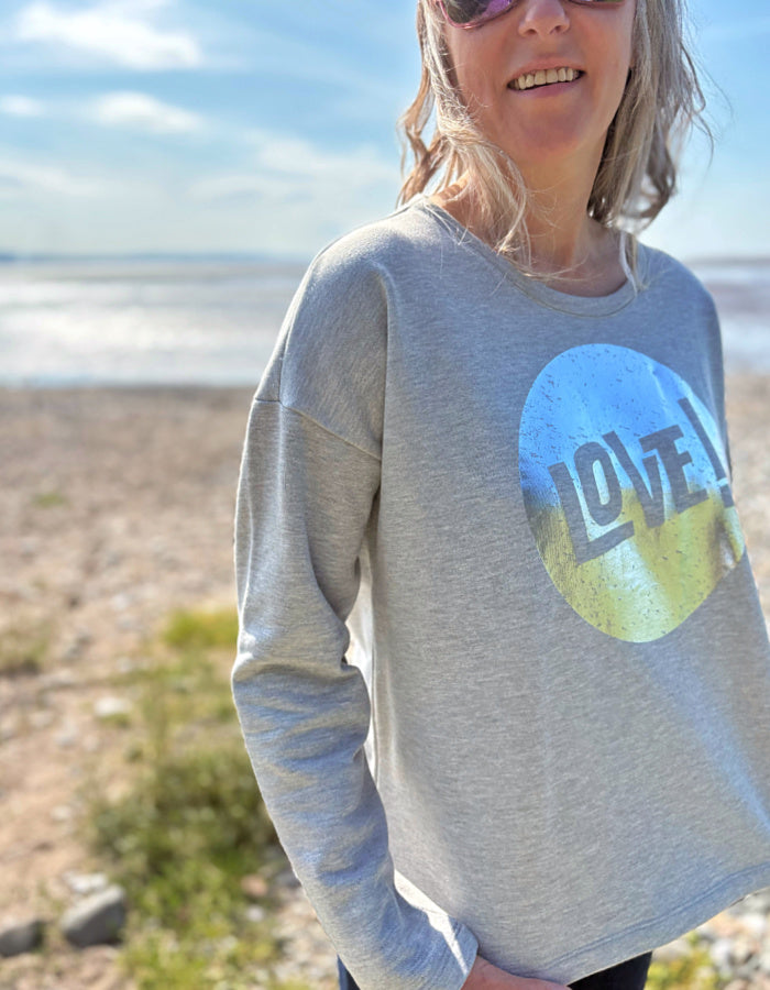 Person wearing a gray sweatshirt with a 'LOVE' graphic in a natural setting