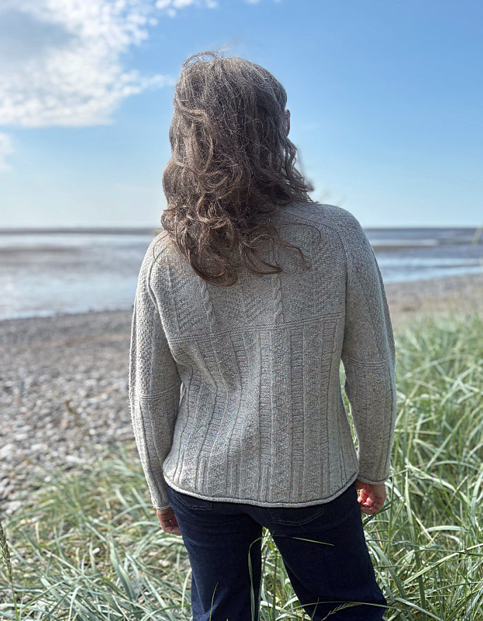 Person wearing a donegal tweed wool grey sweater with wide leg jeans and sunglasses on a beach