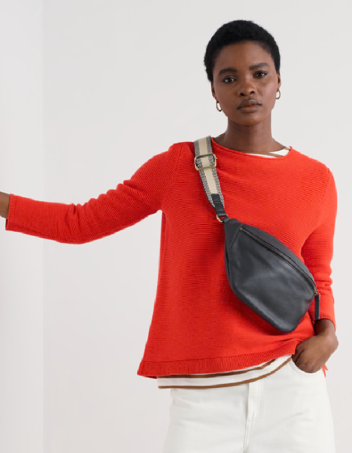 Person wearing a red sweater with a gray crossbody bag on a white background