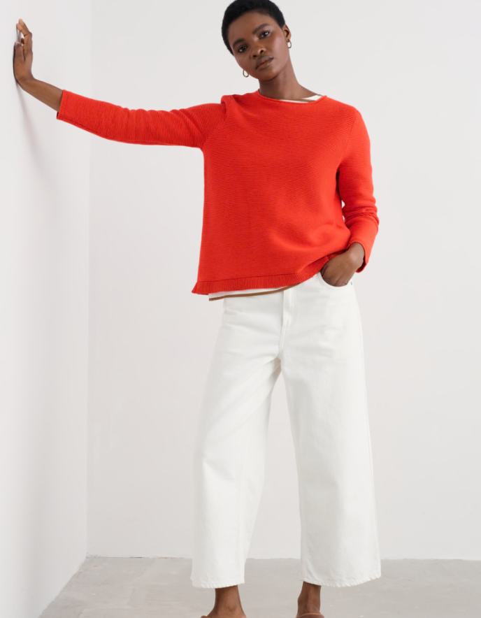 Person wearing a bright red sweater and white pants on a plain background