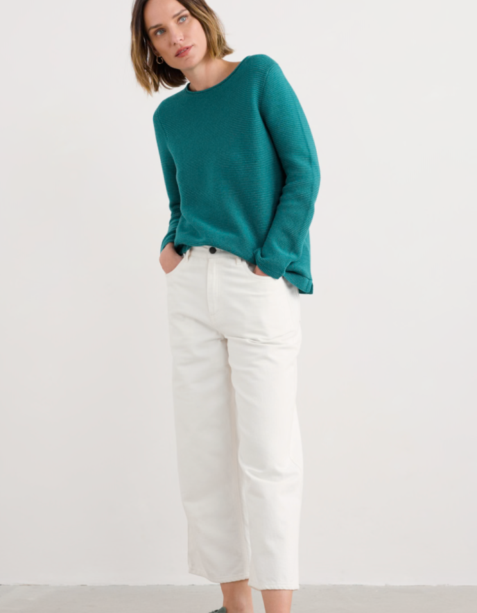 Woman wearing a teal sweater and white pants on a white background
