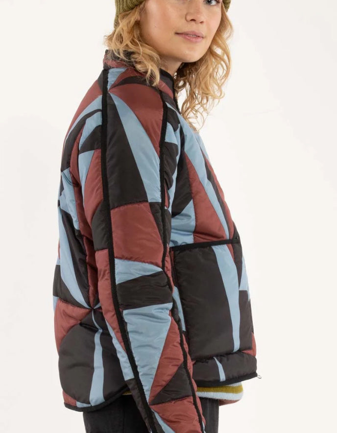 Person wearing a colourful geometric-patterned puffer jacket on a white background