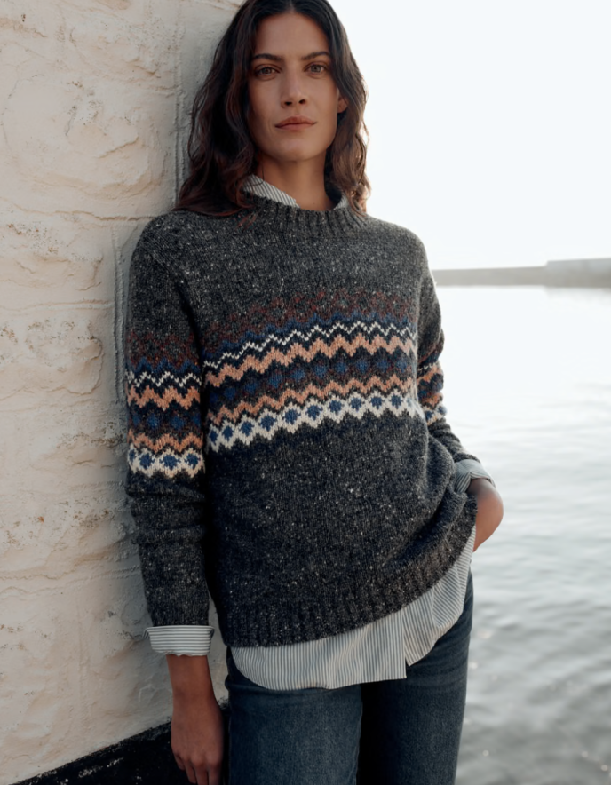 Woman wearing a dark grey tweed sweater with fair isle patterned against a white background