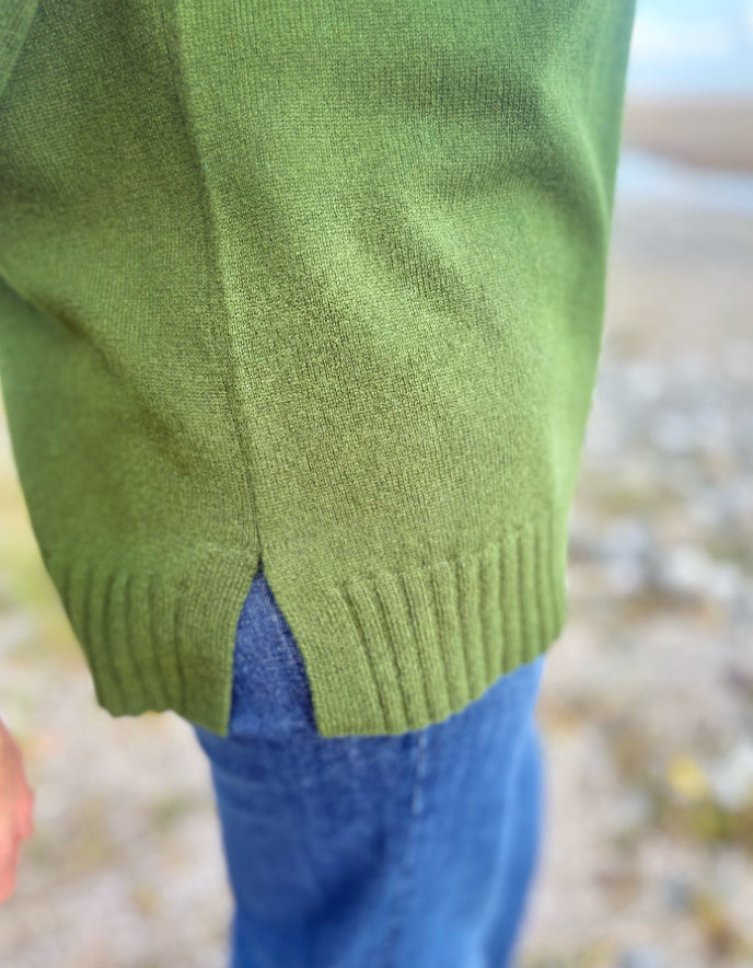 Green sweater sleeve and blue pants against a blurred natural background