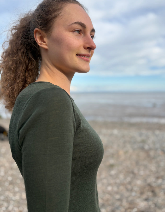 lady wearing fine merino long sleeve t shirt in moss green on a beach
