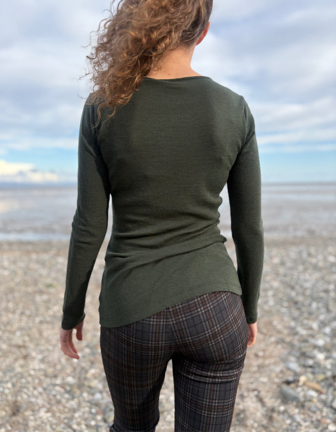 lady wearing fine merino long sleeve t shirt in moss green on a beach
