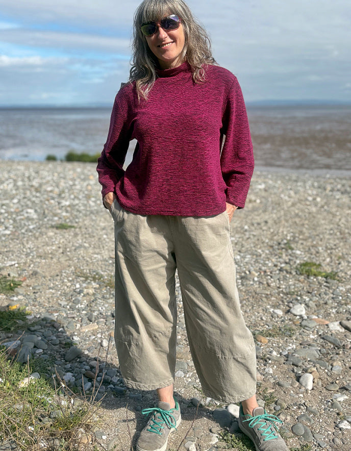 Woman wearing a maroon sweater and sunglasses on a beach with a blue sky.