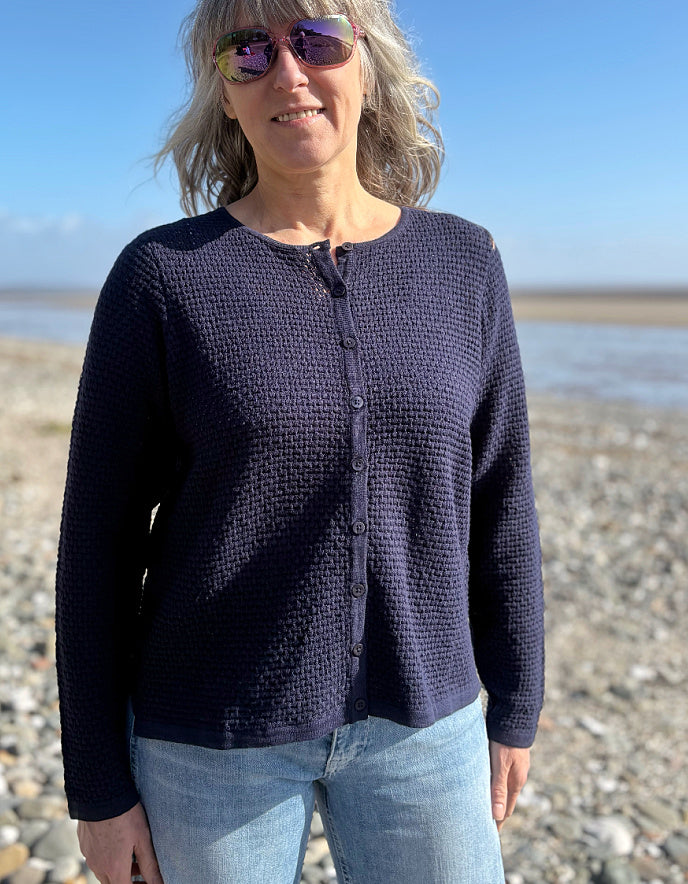 Woman wearing a dark blue cardigan and sunglasses on a beach.
