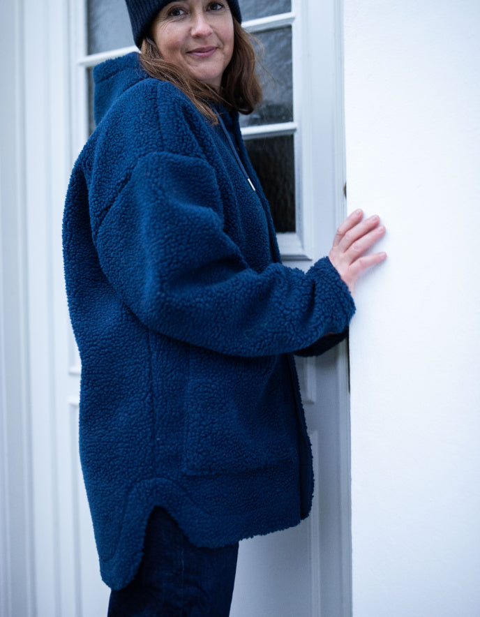 Person wearing a blue fleece jacket standing against a white door.