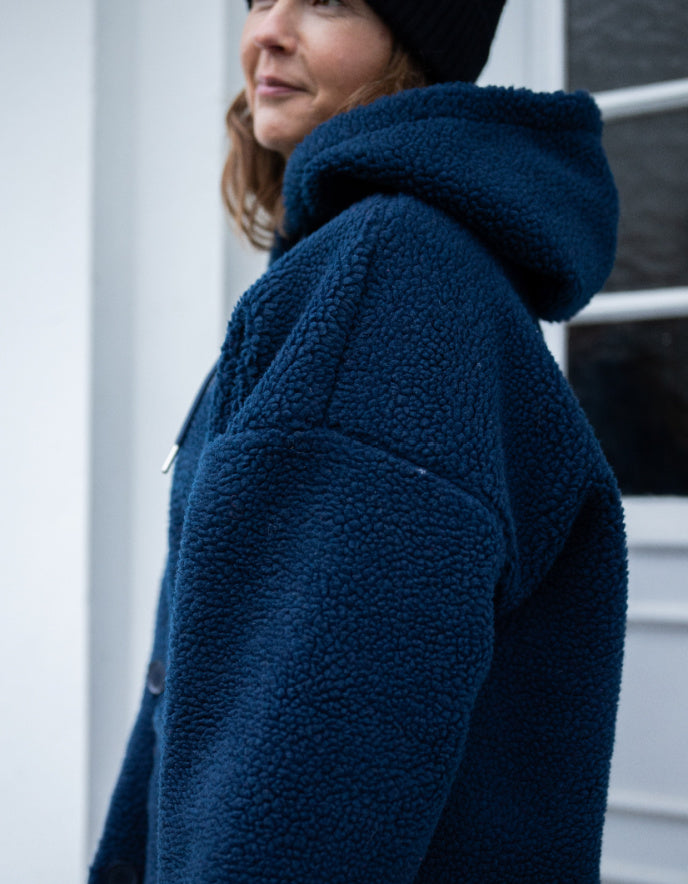 Person wearing a blue fleece jacket with a hood, standing against a neutral background.