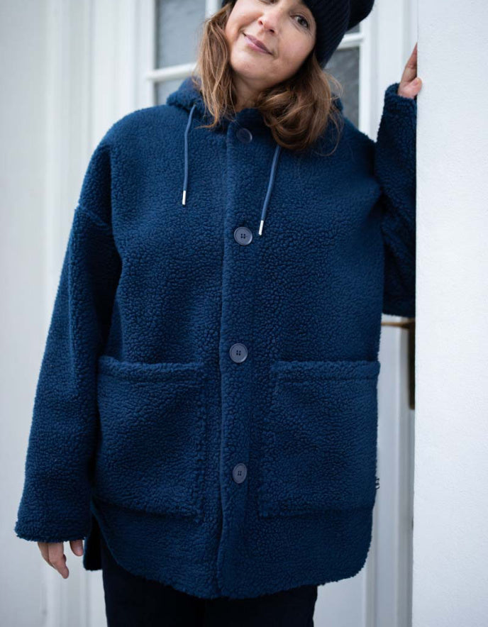 Person wearing a blue coat with a hood, standing against a white door.