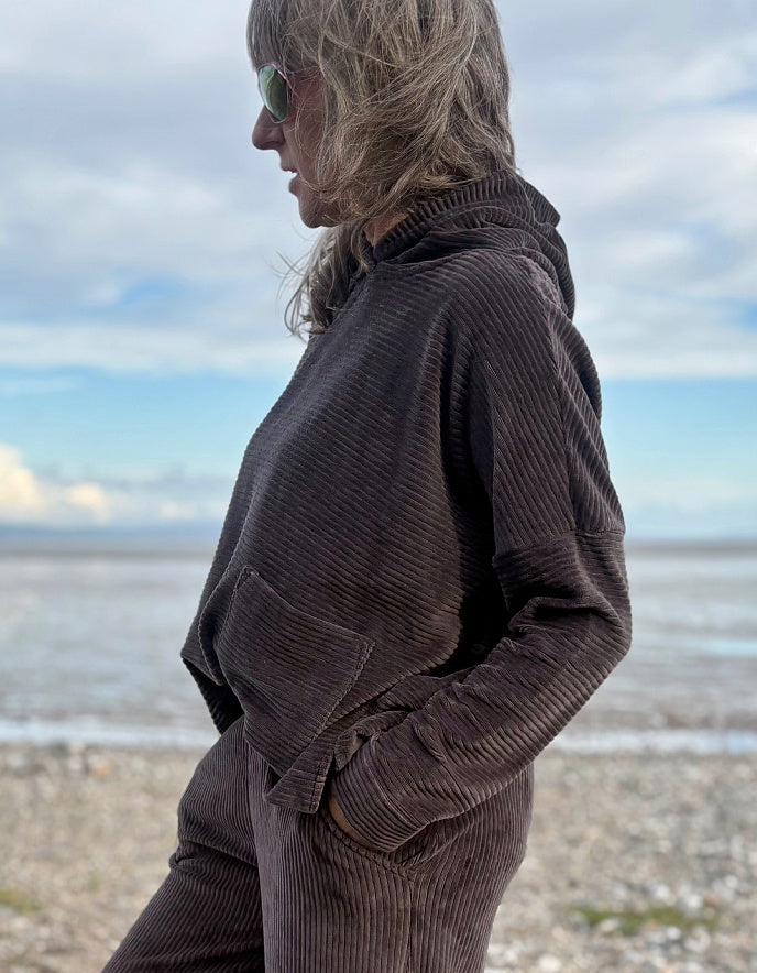 Person wearing a brown cord hooded sweater on a beach with ocean and sky in the background