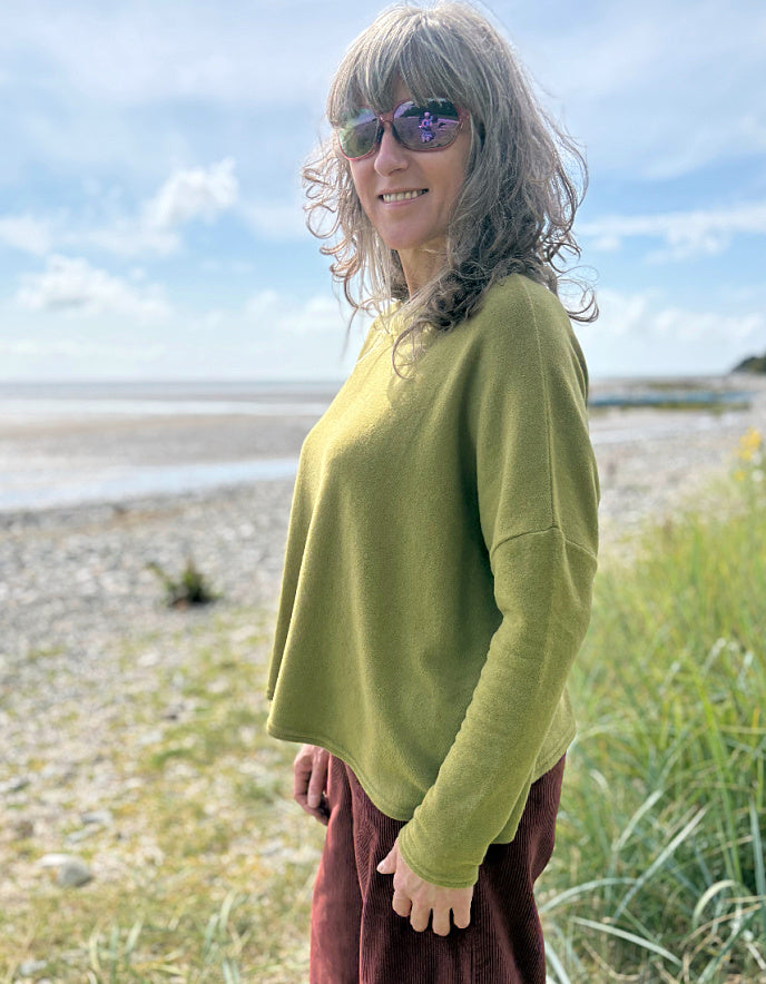 Woman wearing a green sweater and sunglasses standing on a beach.