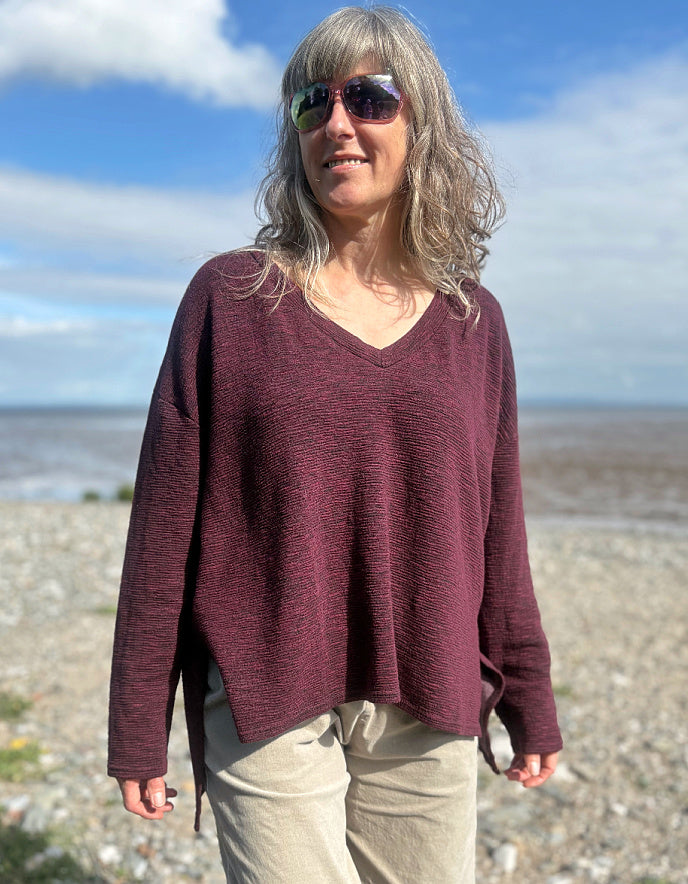 Person wearing a maroon oversized sweater and sunglasses on a beach