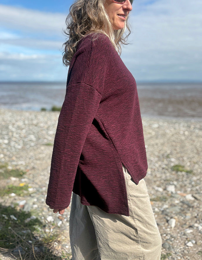 Person wearing a maroon jacket standing on a beach with ocean and sky in the background