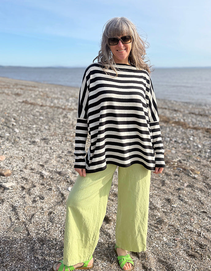 Woman wearing a black and white striped sweater and green pants standing on a beach.