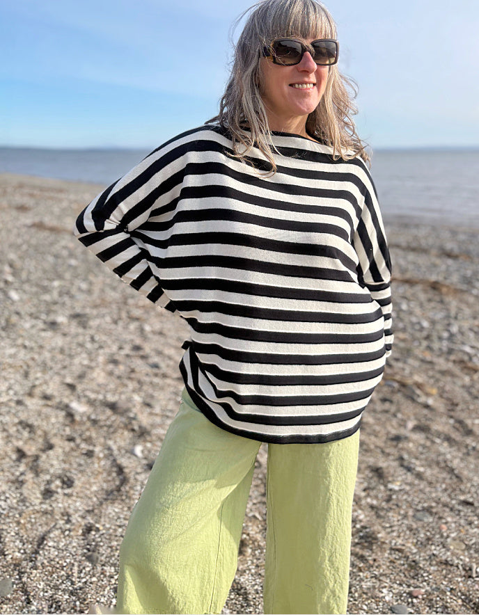 Person wearing a black and white striped sweater and green pants on a beach.