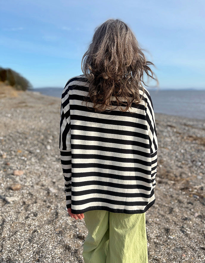 Person wearing a black and white striped sweater on a pebbly beach with ocean view