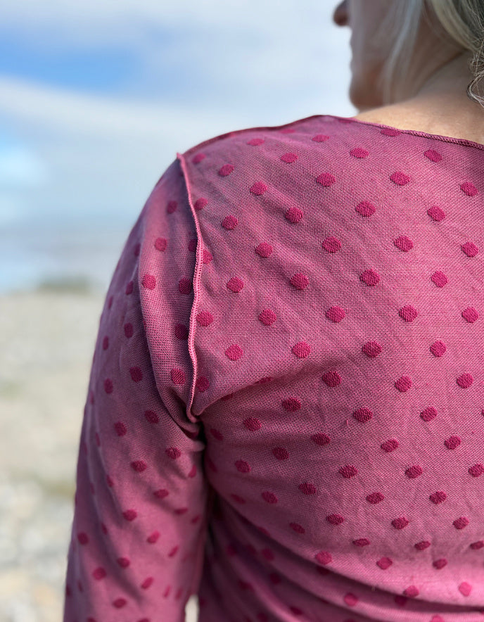 Person wearing a pink polka dot top with a blurred beach background
