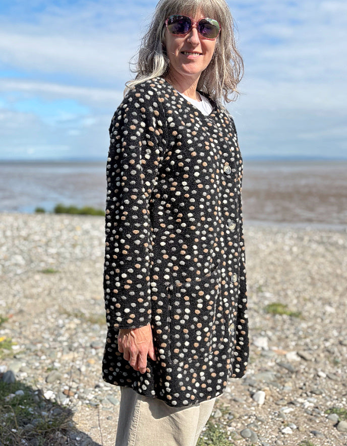 Woman wearing a black polka dot coat on a beach