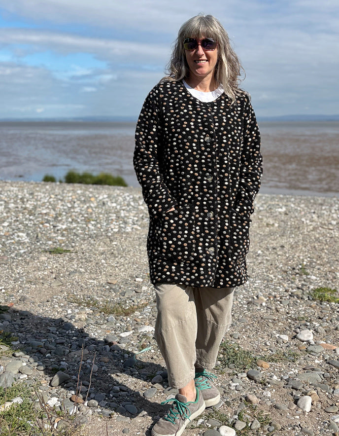 Woman standing on a pebbly beach with water and sky in the background