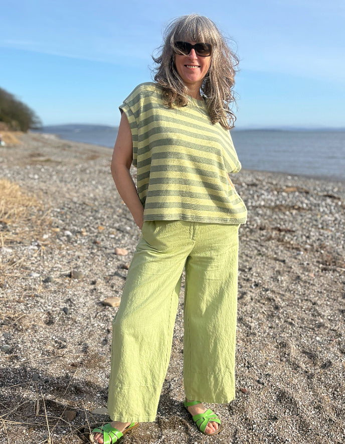 Woman in a striped shirt and green pants standing on a beach.