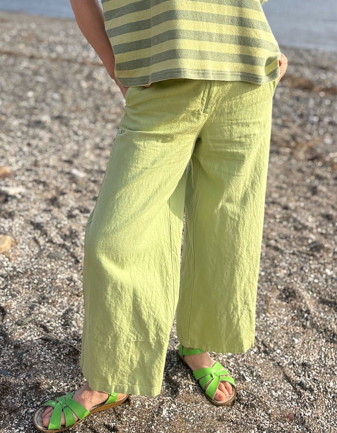 Person wearing green striped shirt and wide-leg pants on a beach.