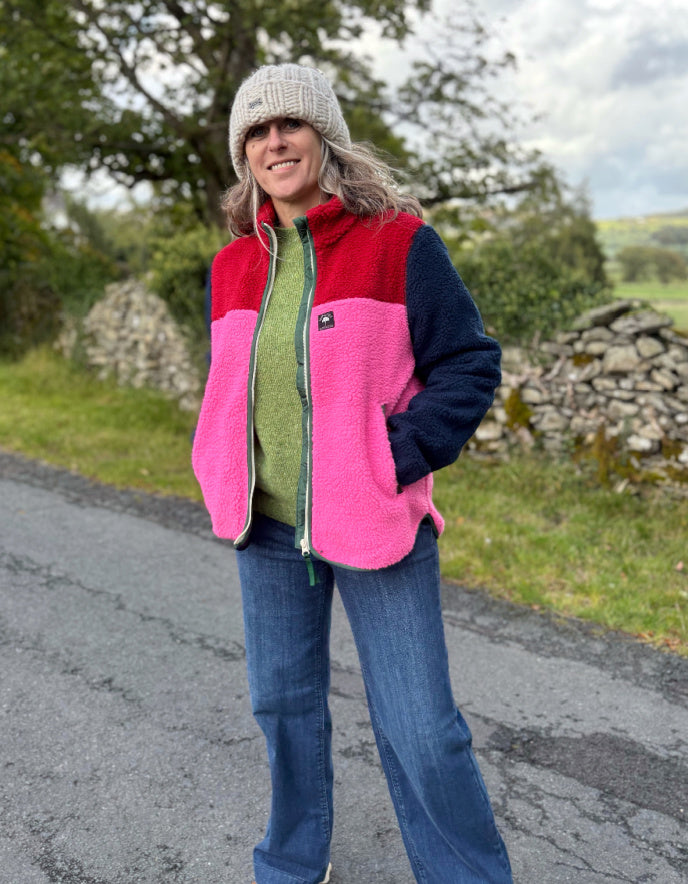 Person wearing a colorful jacket standing on a road with greenery in the background