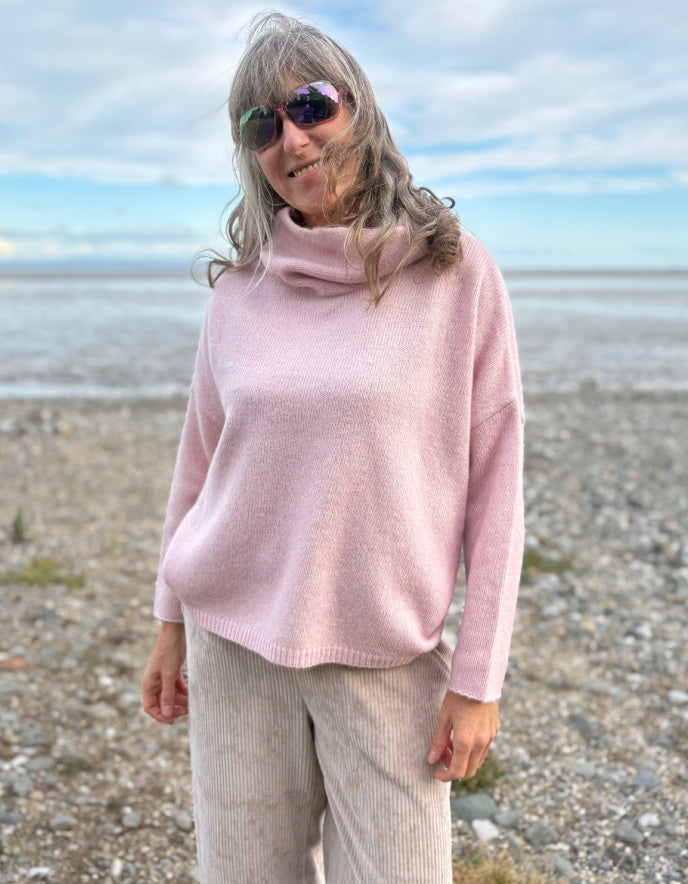 Person wearing a pink sweater and sunglasses on a beach